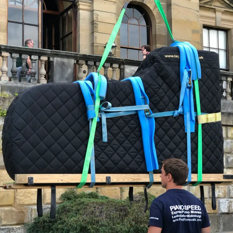 A piano lifted on padded straps by a specialist crew